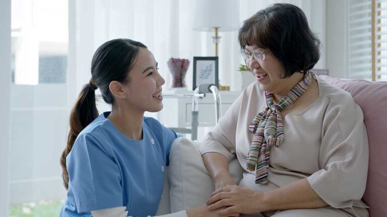 Older adults share a quiet conversation at a table in a bright assisted living common room.